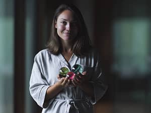 A candid full-body photo of a Caucasian woman standing in soft morning light, wearing light, cozy morning clothes (like a robe or oversized shirt), gently holding in her hand two or three elegant, smooth glass-like spheres with a shiny surface, colorful and translucent, natural smile, relaxed posture, indoors near a window, calm and bright atmosphere, warm tones, soft background blur, cinematic photography, realistic lighting, subtle shadows